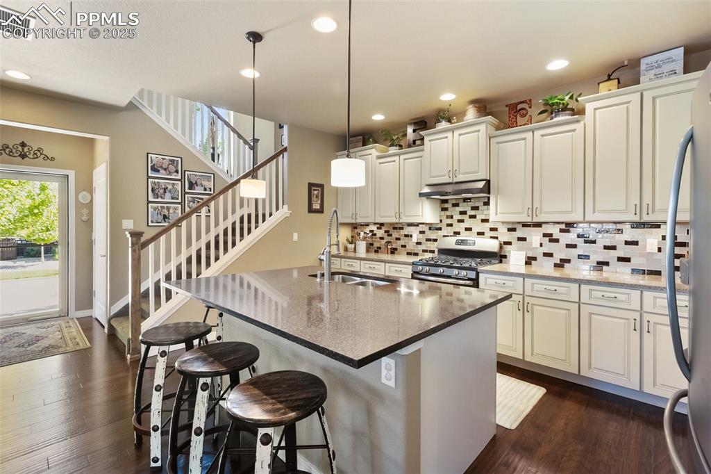 Image 16 of 50: Kitchen with stainless steel gas stove, under cabinet range hood, decorativ
