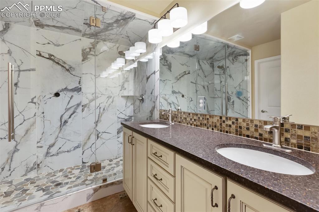 Image 24 of 50: Bathroom with a marble finish shower, double vanity, decorative backsplash,