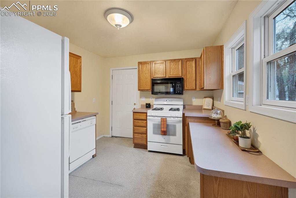 Image 10 of 16: Kitchen with white appliances, light countertops, brown cabinets, and light