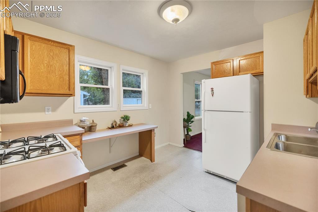 Image 9 of 16: Kitchen with white appliances, light countertops, and brown cabinetry