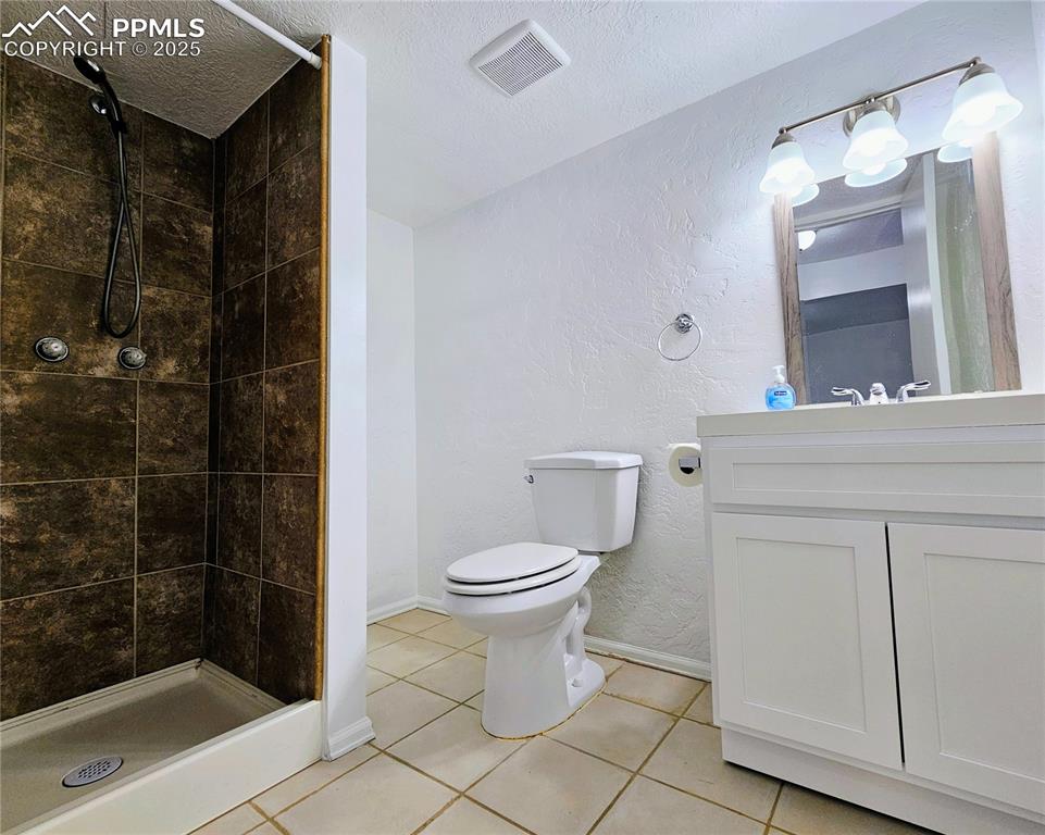 Image 27 of 31: Full bath with a textured wall, light tile patterned floors, vanity, a show
