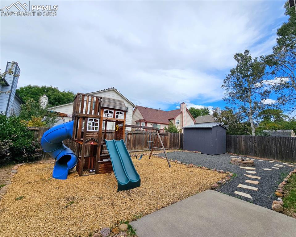 Image 30 of 31: View of jungle gym featuring a fenced backyard, a fire pit, and a storage s