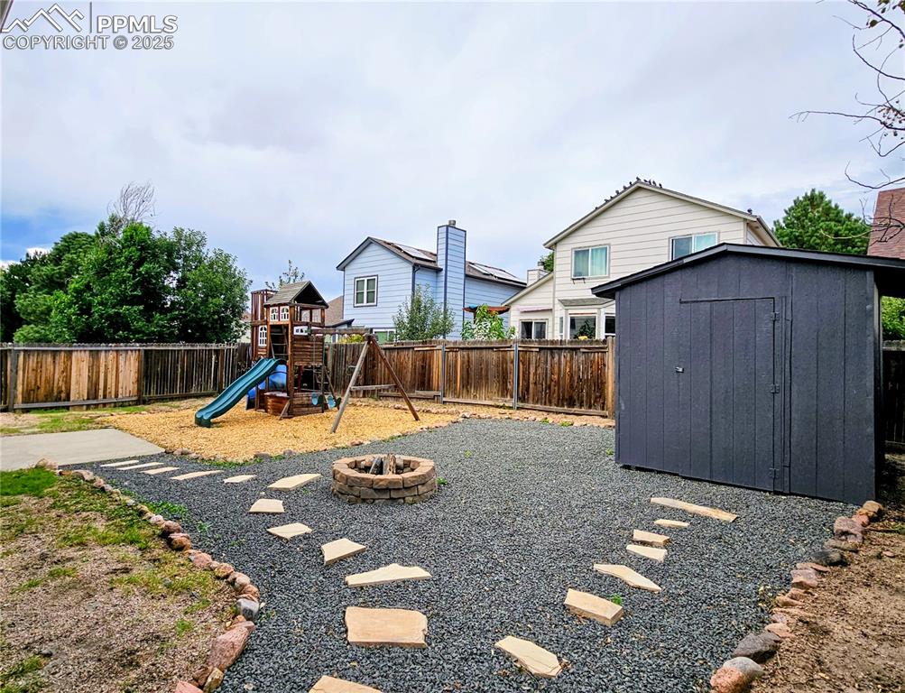 Image 4 of 31: Fenced backyard with a fire pit, a shed, and a playground