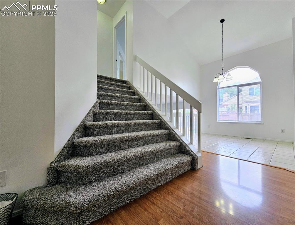 Image 6 of 31: Stairway featuring wood finished floors, a chandelier, and high vaulted cei