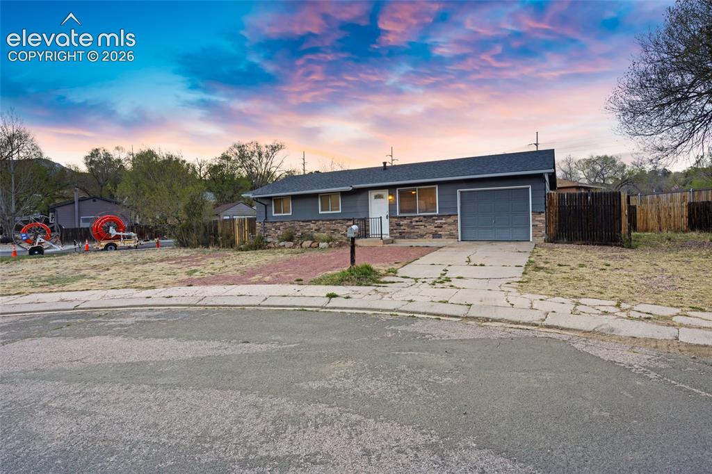 Caption: Ranch-style residence featuring a dark gray exterior, a stone veneer accent, and a dark asphalt shin
