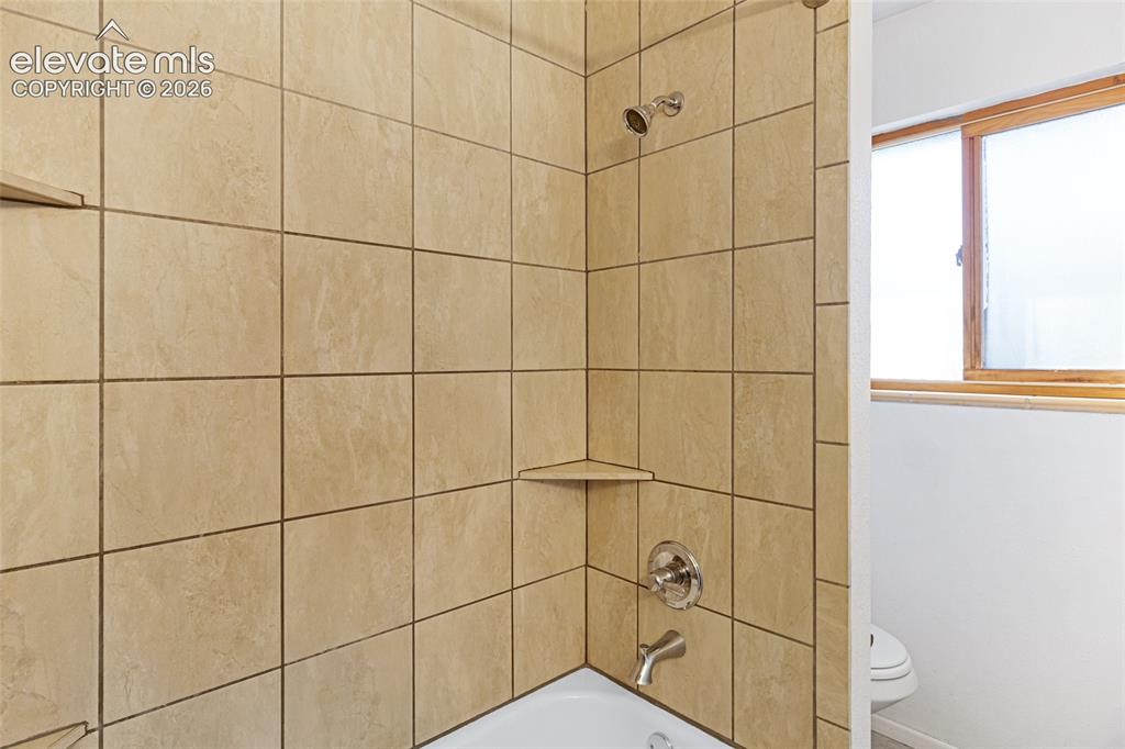 Image 13 of 20: Tiled shower enclosure featuring neutral stone-finish ceramic tiles, chrome