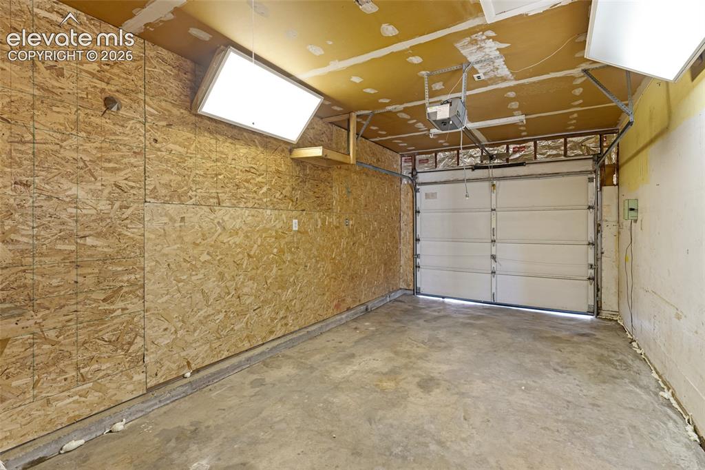 Image 17 of 20: Spacious garage featuring concrete flooring, OSB-sheathed walls, overhead l
