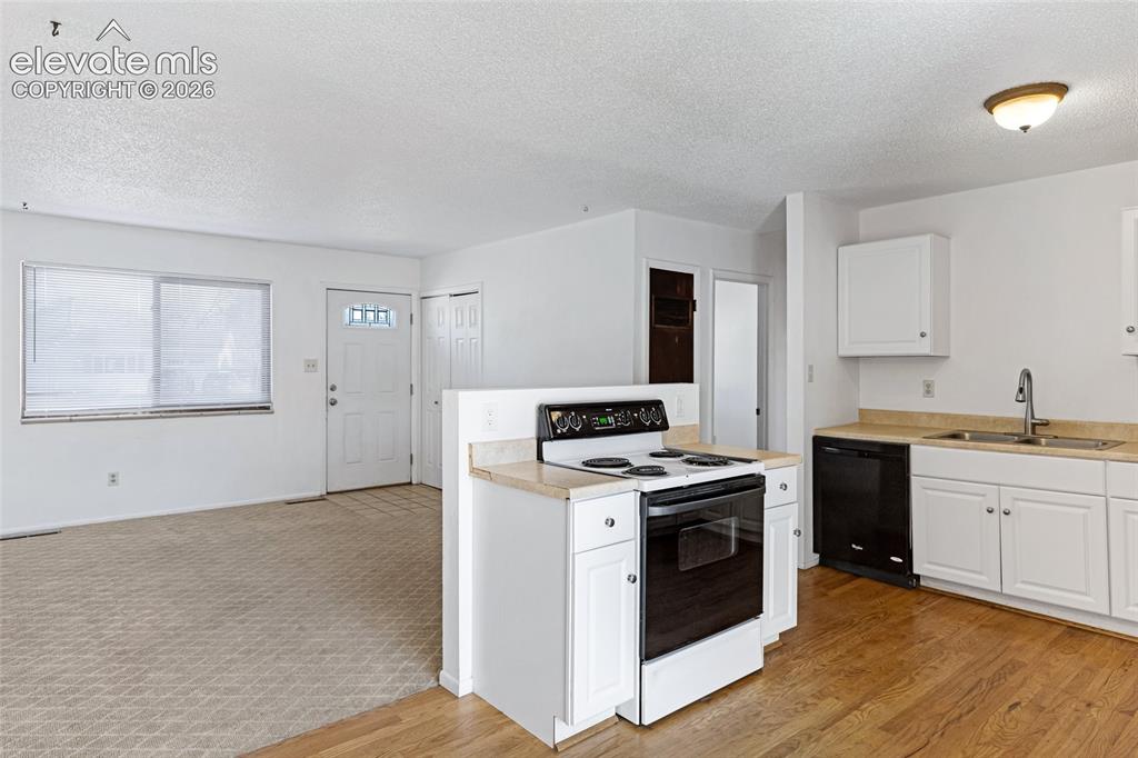 Image 7 of 20: Bright kitchen featuring wood-finish flooring, white cabinetry, a black ran