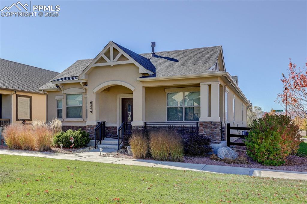 Caption: View of front of property with stone siding, stucco siding, a front yard, and covered porch