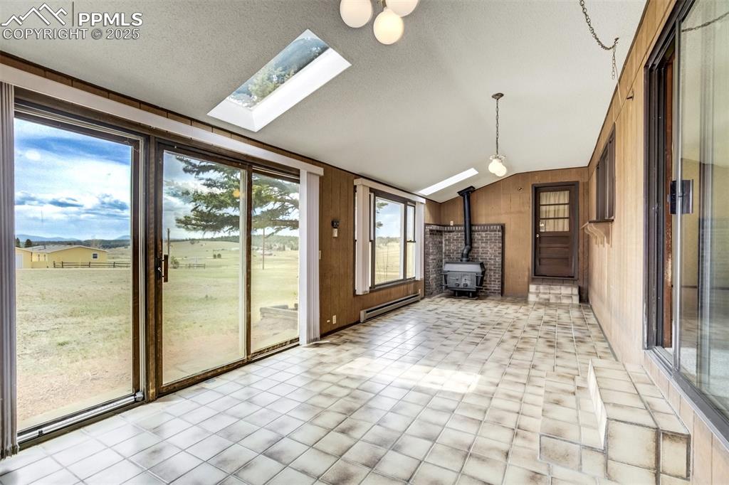 Image 19 of 43: Sunroom with second woodburning stove, tile flooring, and door to the garag