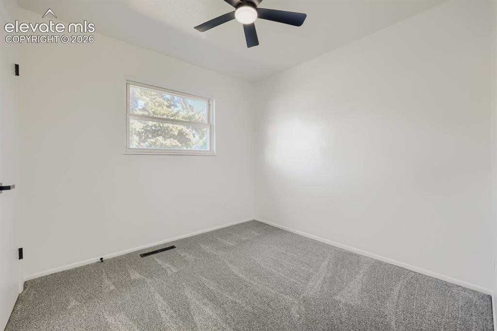 Image 14 of 22: Room with light gray carpeting, white walls, and a black ceiling fan