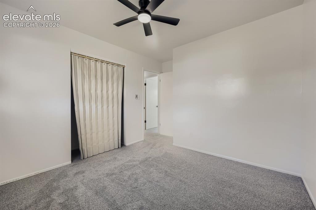 Image 17 of 22: Plush grey carpeting, white painted walls, and a black ceiling fan with int