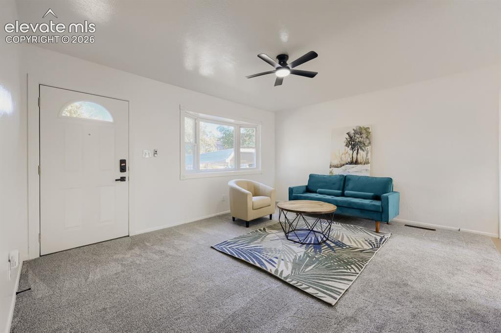 Image 4 of 22: Bright, open living space featuring neutral carpeting, a ceiling fan with i