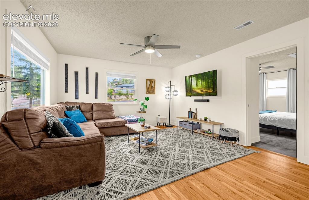 Image 18 of 46: Hardwood flooring, white walls, large windows, ceiling fan with integrated 