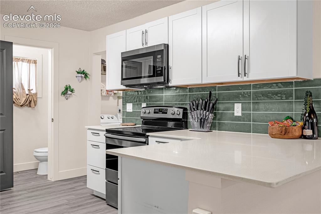 Image 21 of 46: White upper and lower cabinetry, dark green subway tile backsplash, light-t