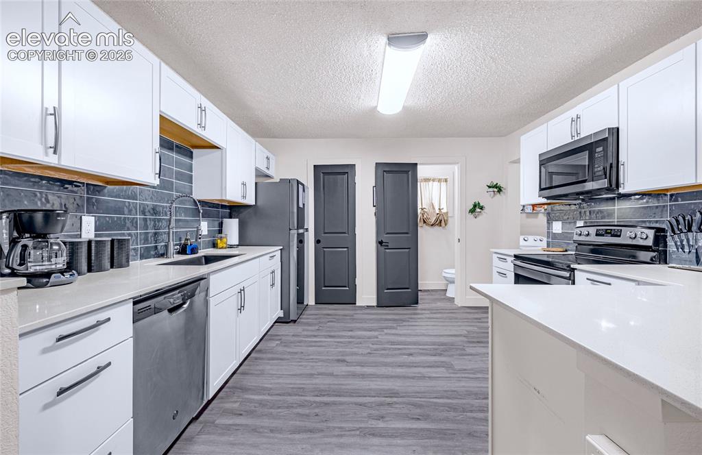 Image 36 of 46: Kitchen featuring white cabinetry, light-toned countertops, a dark subway t