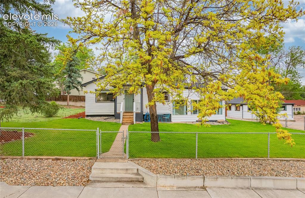 Image 40 of 46: White exterior siding, front entry stairs, fenced front yard, mature trees,