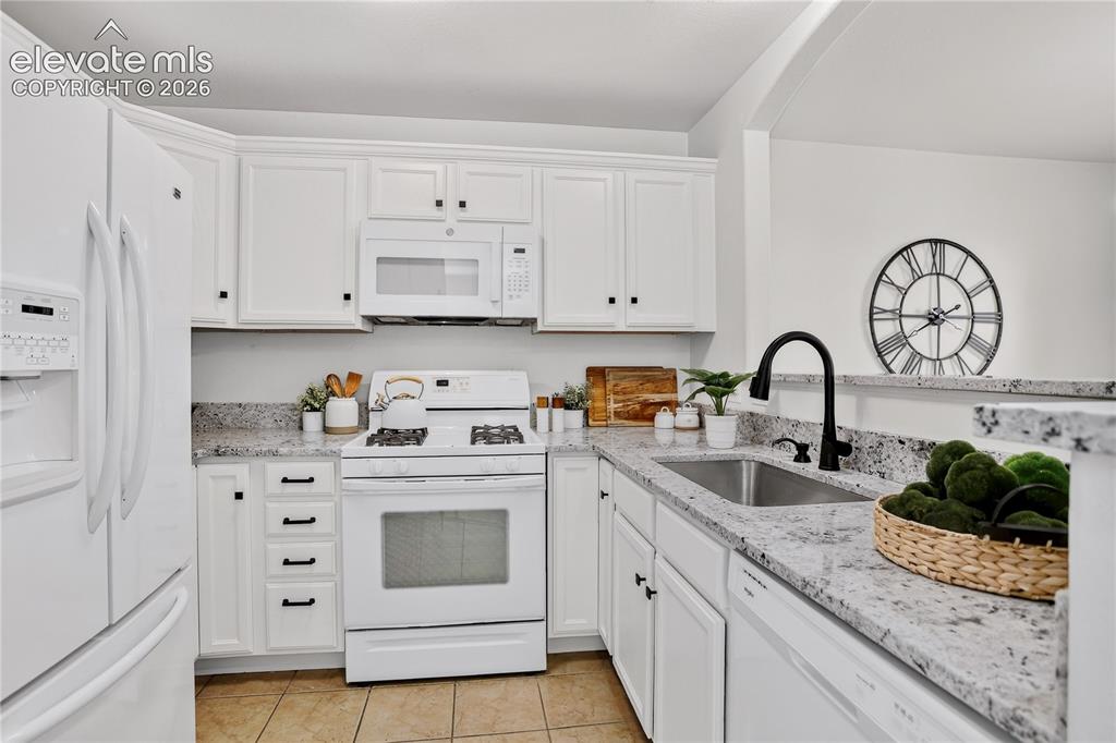 Image 4 of 35: Kitchen with tile floors, white appliances, and quartz countertops. 