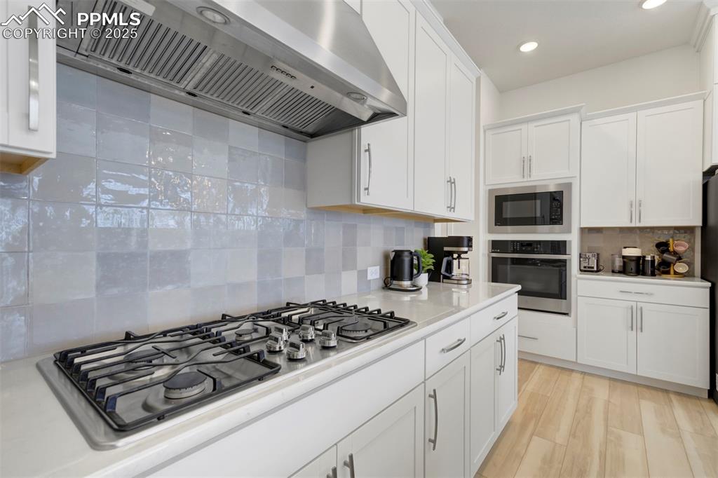 Image 20 of 45: Kitchen featuring ventilation hood, stainless steel appliances, tasteful ba