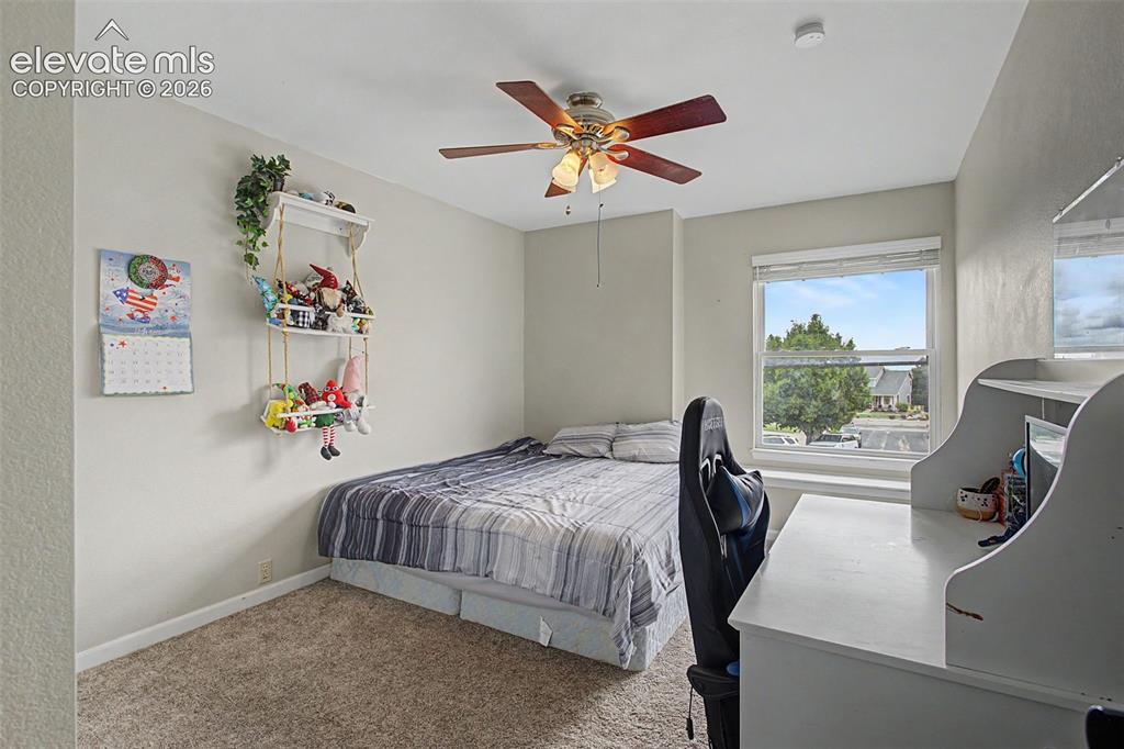 Image 28 of 45: Carpeted room featuring a ceiling fan with light fixture, a window with bli