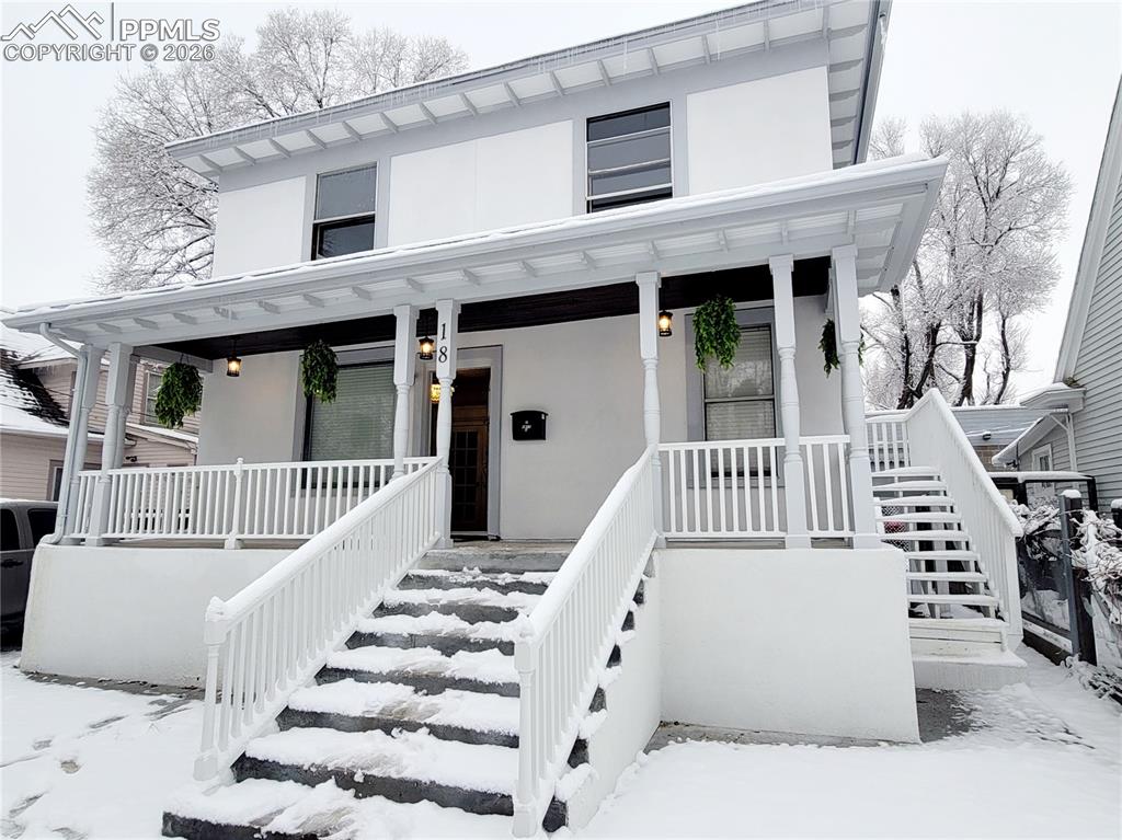 Caption: Two-story residential structure featuring a covered front porch with white railings and columns