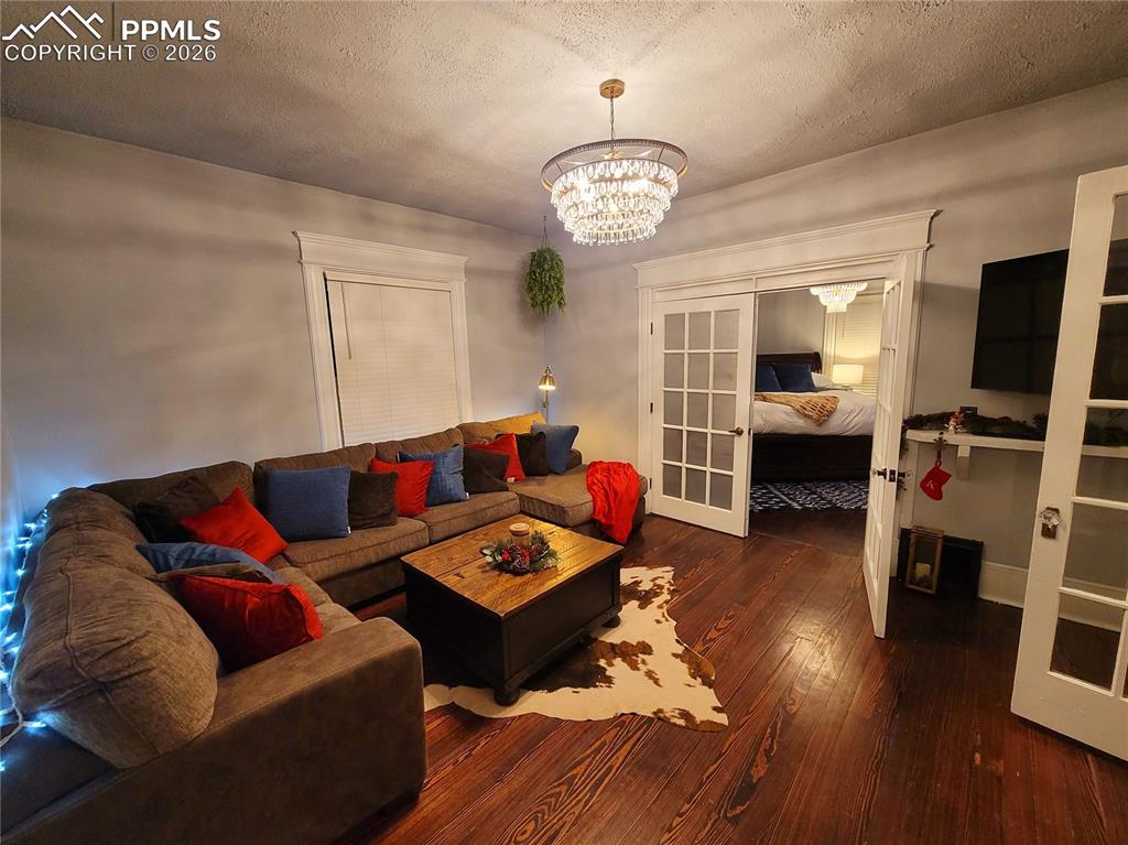 Image 4 of 21: Living area with wood-finish flooring, a tiered crystal chandelier, and whi