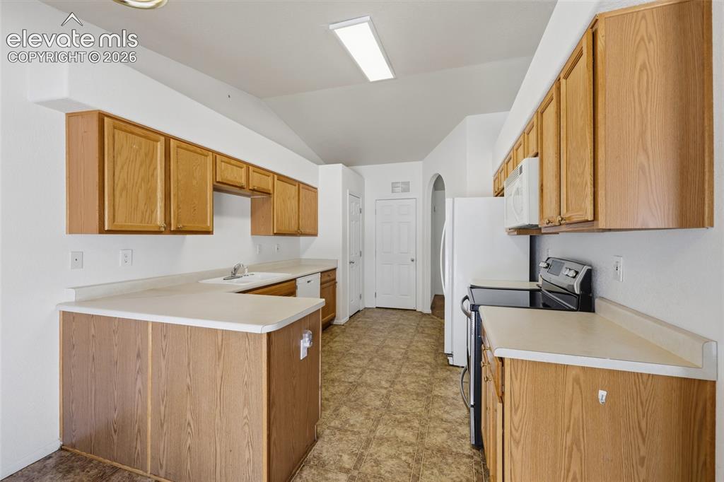 Image 17 of 45: Kitchen featuring wood-finish cabinetry, light-toned countertops, vaulted c