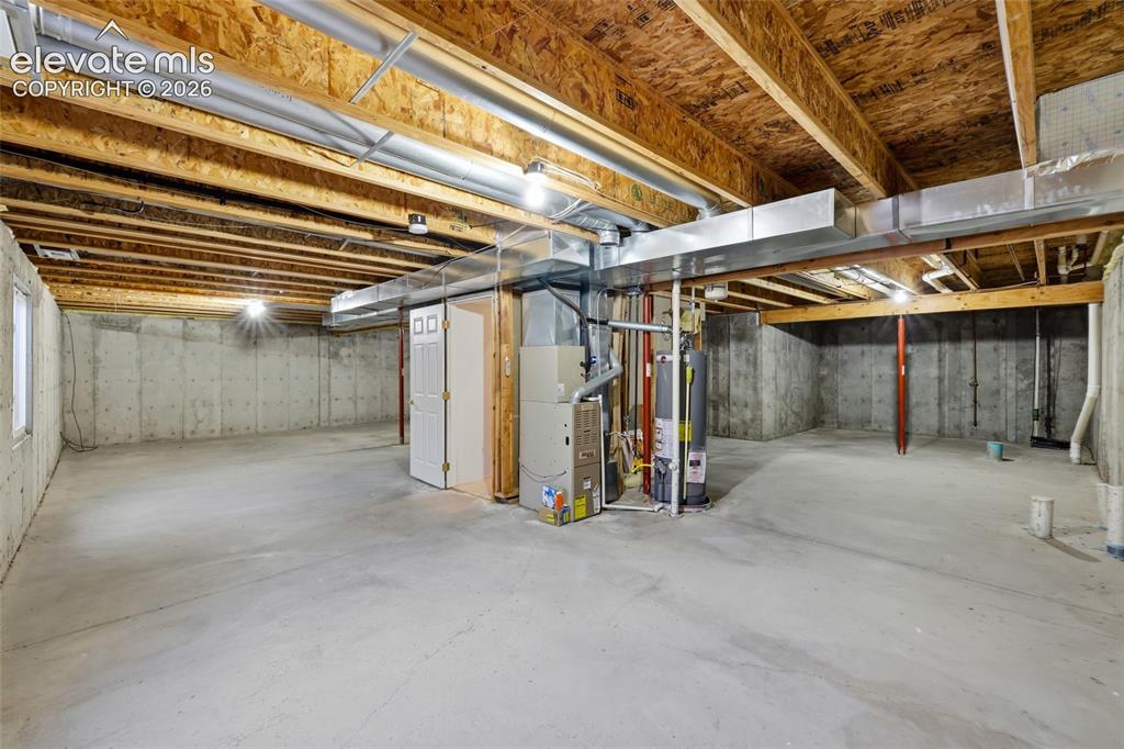 Image 31 of 45: Unfinished basement with concrete flooring, exposed ceiling joists, and a u