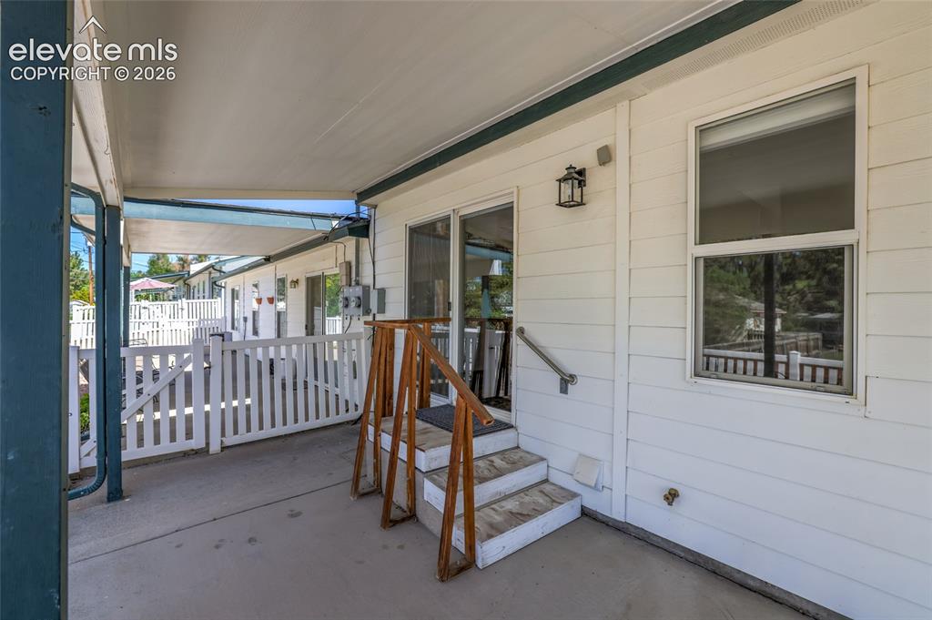 Image 37 of 45: Covered patio with concrete flooring, white picket fencing, and a glass sli