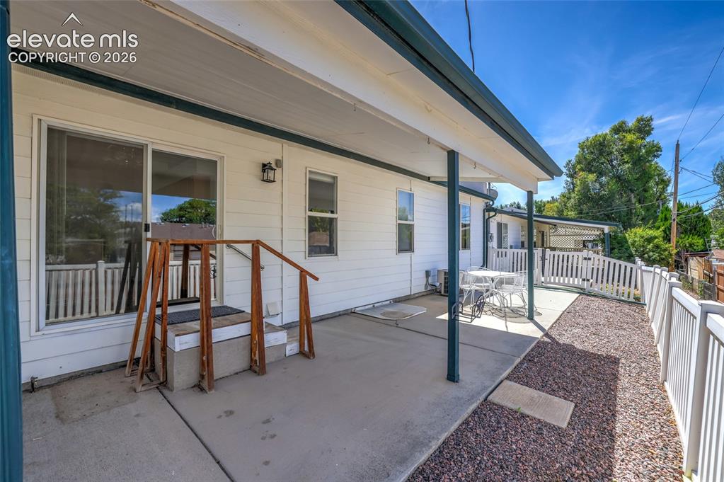Image 38 of 45: Covered concrete patio with white siding exterior and multiple windows