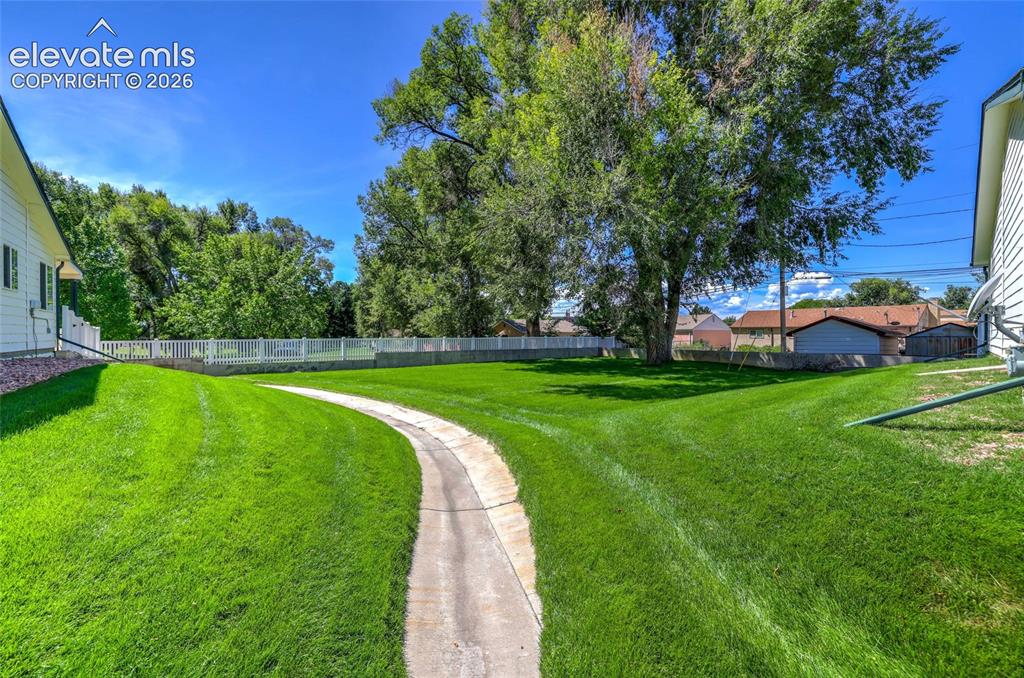 Image 41 of 45: Expansive lawn with mature trees, a curving concrete pathway, and a white p
