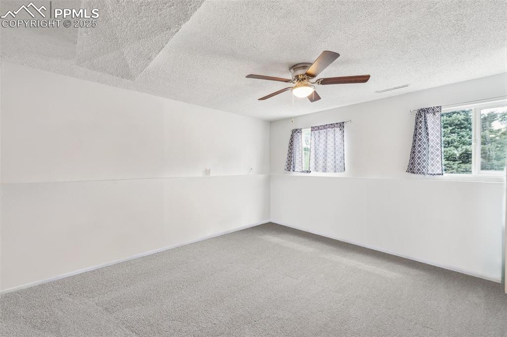 Image 9 of 19: Lower-level fourth bedroom with neutral tones and ceiling fan.
