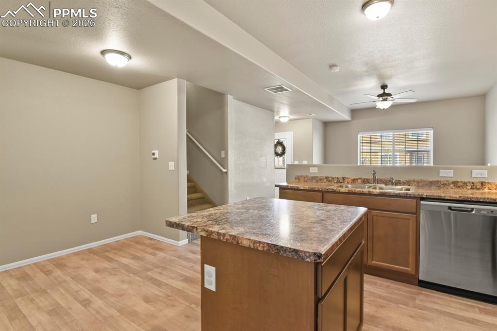 Image 10 of 27: The kitchen features an island, brown cabinetry, a stainless steel dishwash