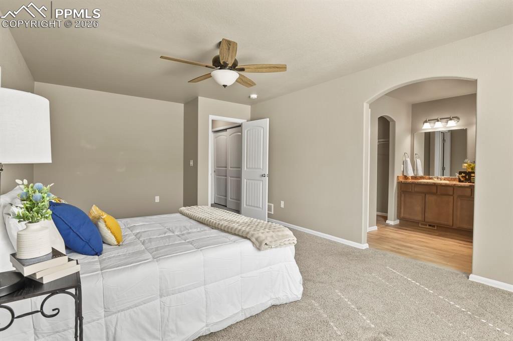 Image 14 of 27: This bedroom features carpeted flooring, a ceiling fan, and an arched doorw