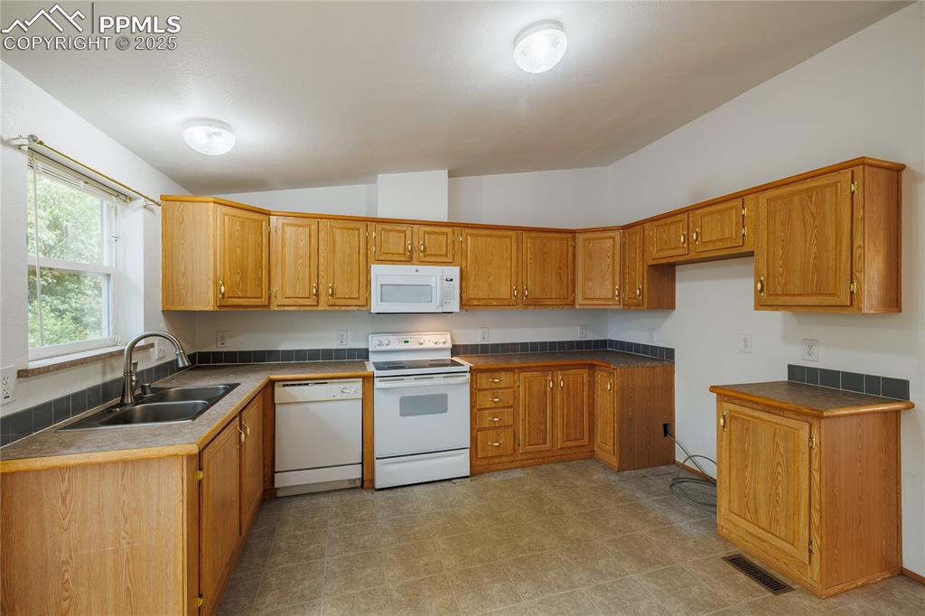 Image 8 of 26: Kitchen with white appliances, lofted ceiling, brown cabinetry, and dark co