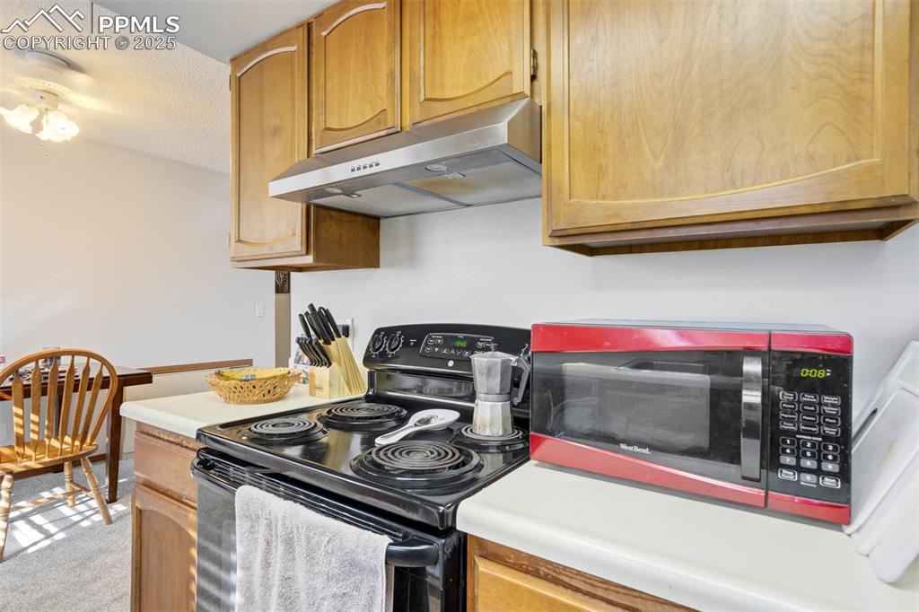 Image 16 of 35: Kitchen with black electric range, light countertops, under cabinet range h