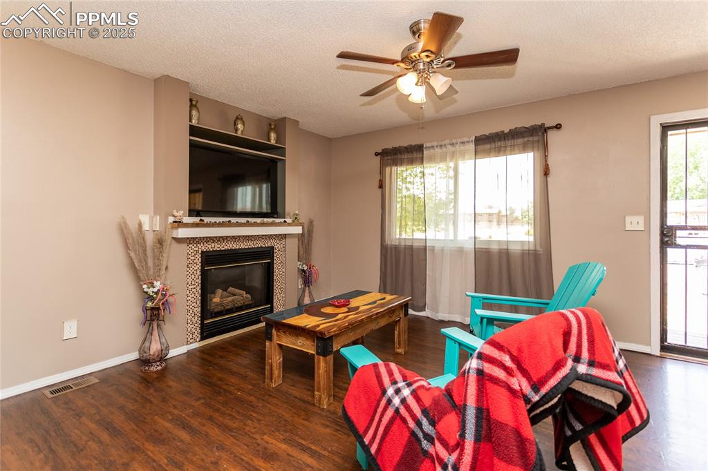 Image 34 of 50: Living area with wood finished floors, ceiling fan, baseboards, a tile fire