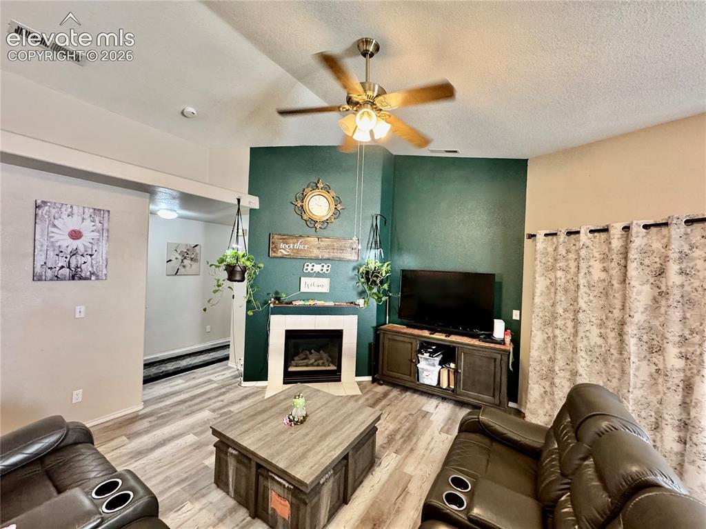 Image 13 of 32: Living area featuring a corner fireplace with a mantel, wood-finish floorin