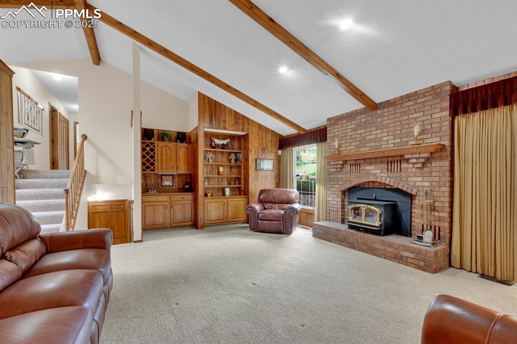 Image 14 of 47: Living room featuring beam ceiling, wooden walls, light carpet, a wood stov