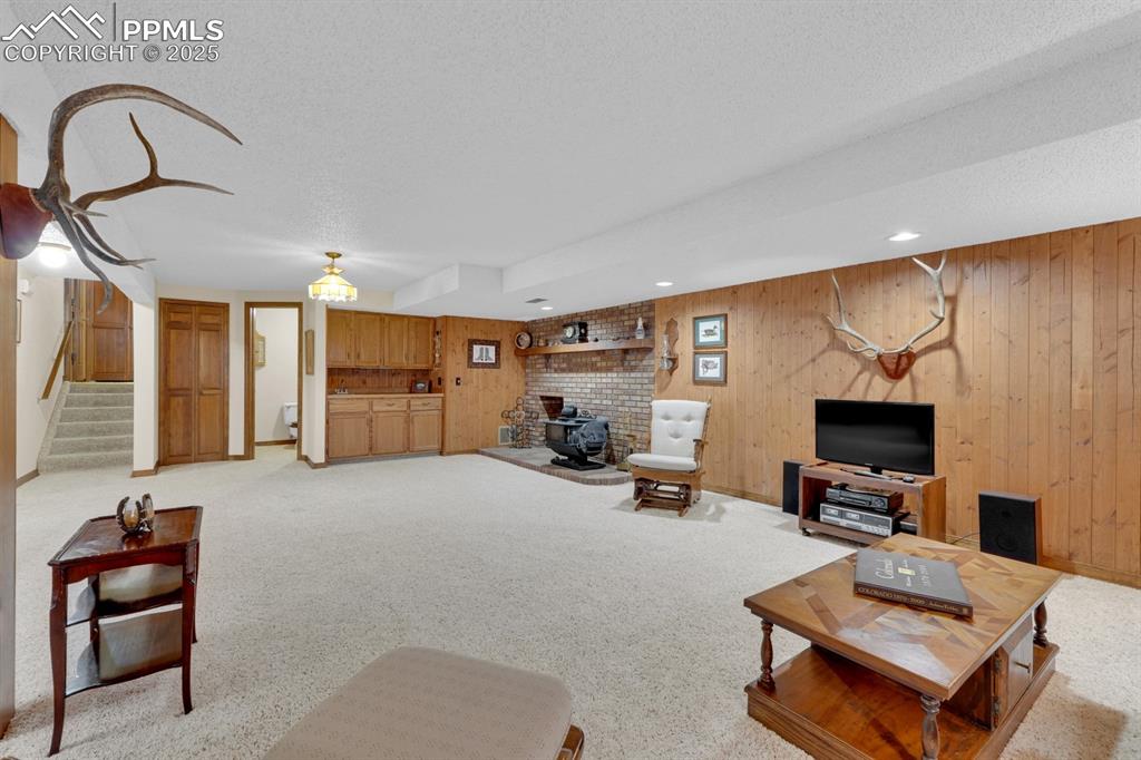 Image 30 of 47: Living area with a wood stove, light colored carpet, stairs, wood walls, an