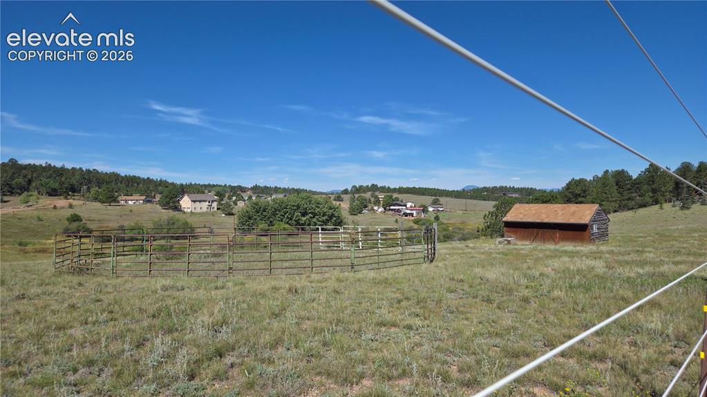 Image 6 of 35: Expansive outdoor space featuring a metal corral, a rustic wooden outbuildi