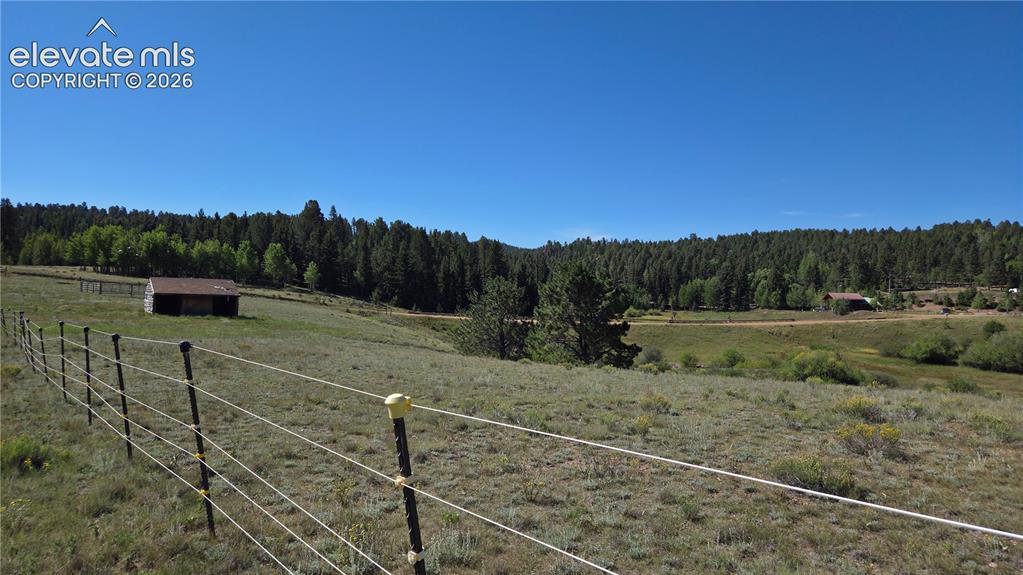 Image 8 of 35: Expansive open land with a rustic horse stall, perimeter fencing.