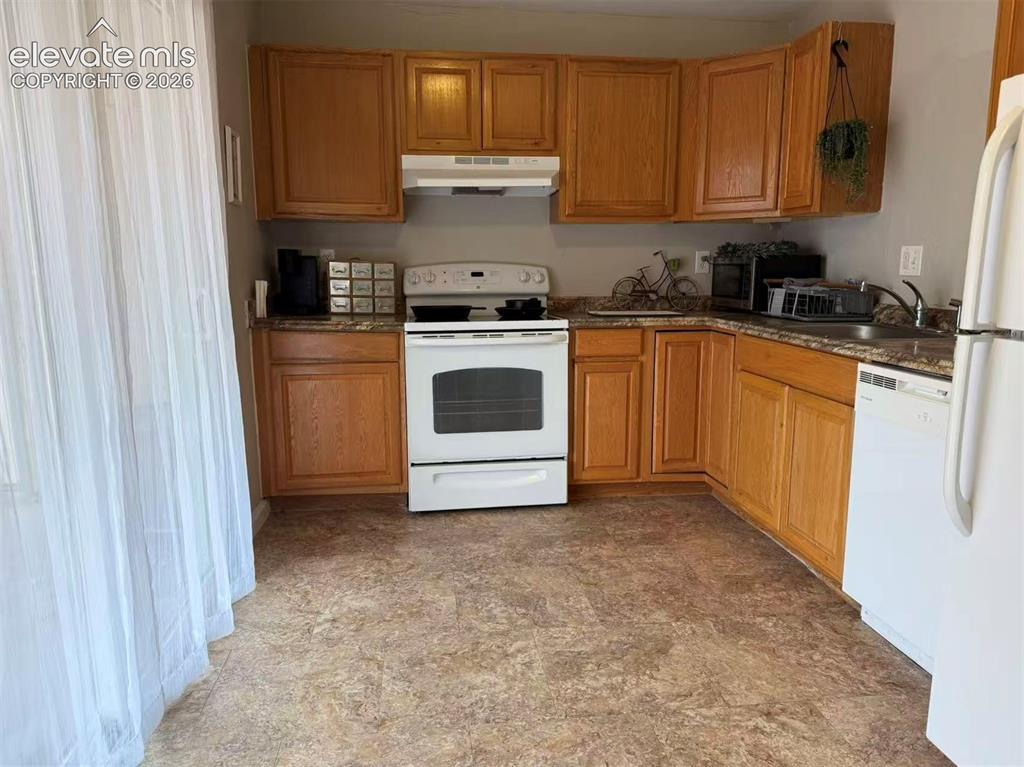Image 4 of 11: Kitchen featuring wood cabinetry, solid surface countertops, white applianc