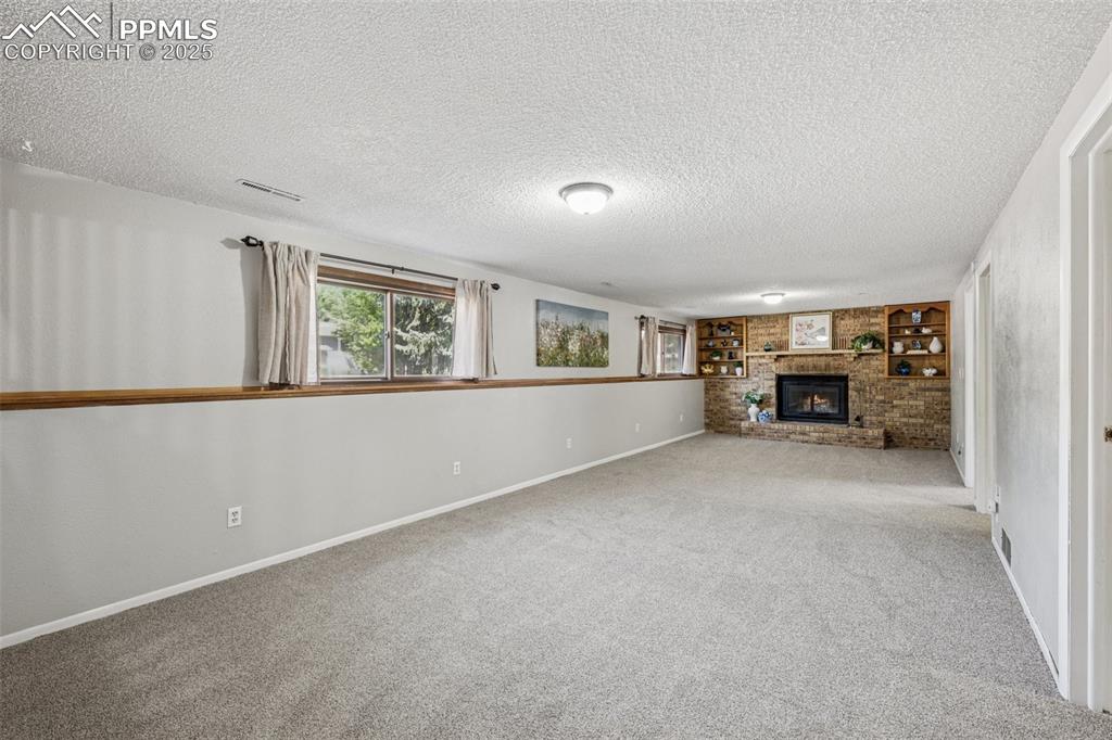 Image 24 of 44: Lower level family room with wood burning, new carpet, fireplace and built