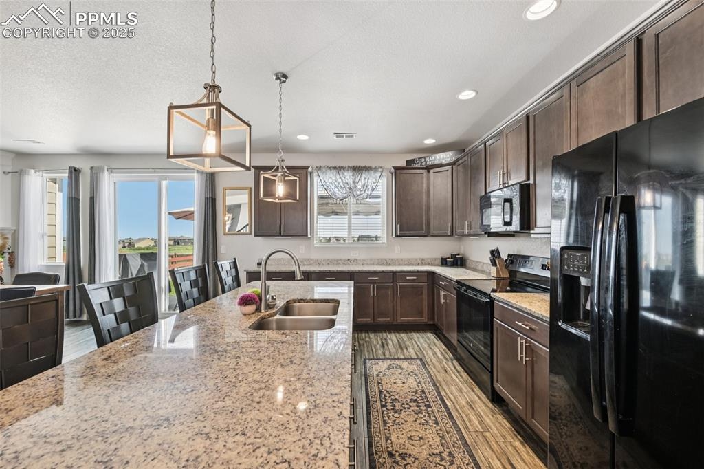 Image 15 of 44: Kitchen featuring black appliances, dark brown cabinets, light stone counte