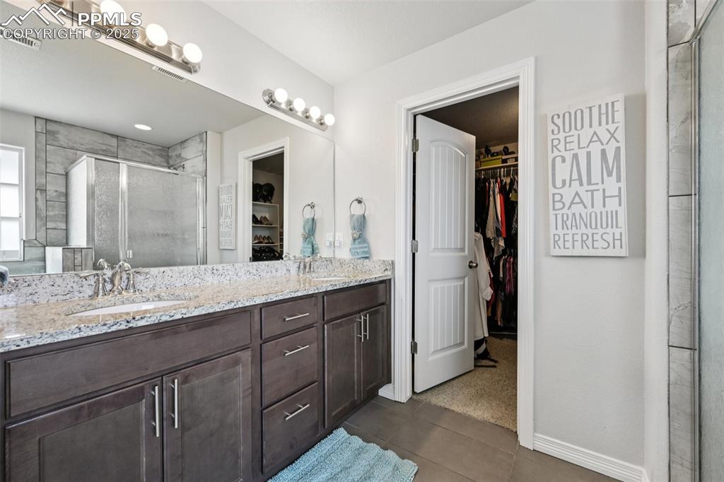 Image 27 of 44: Full bathroom featuring a walk in closet, double vanity, a shower stall, an