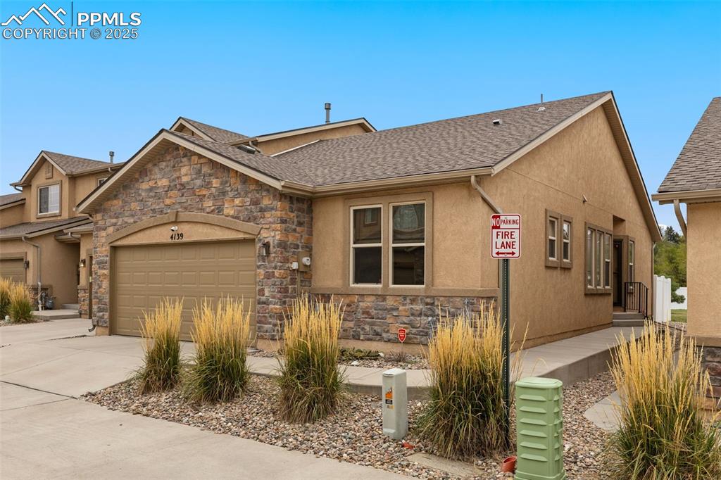 Image 1 of 33: View of front facade with stone siding, driveway, stucco siding, an attache