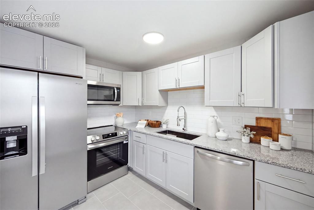 Image 6 of 26: Stainless steel appliances, white shaker-style cabinetry, granite-patterned