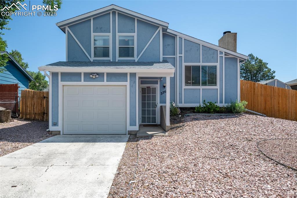 Caption: View of front of home with a chimney, stucco siding, a garage, and concrete driveway
