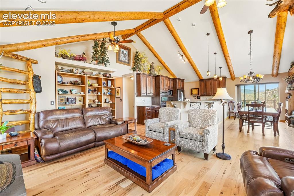 Image 11 of 50: Open concept living room with tall vaulted-wood beamed ceilings, a wood bur